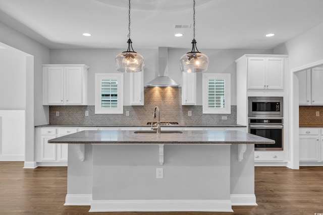 kitchen with wall chimney range hood, visible vents, appliances with stainless steel finishes, a sink, and dark stone countertops