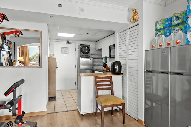 kitchen with freestanding refrigerator, white cabinetry, stacked washer / drying machine, and ornamental molding