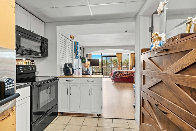 kitchen featuring arched walkways, black appliances, light tile patterned flooring, a drop ceiling, and white cabinetry