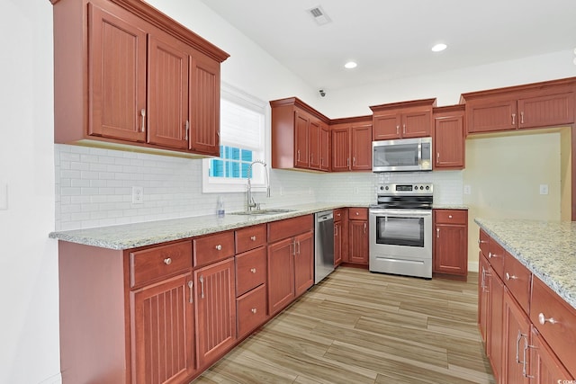 kitchen featuring tasteful backsplash, recessed lighting, light stone counters, appliances with stainless steel finishes, and a sink