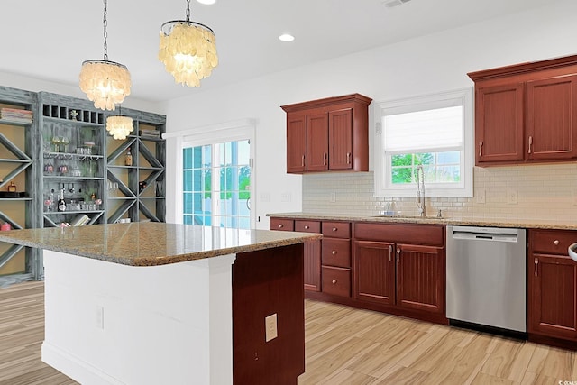 kitchen featuring stainless steel dishwasher, stone counters, backsplash, a sink, and a notable chandelier