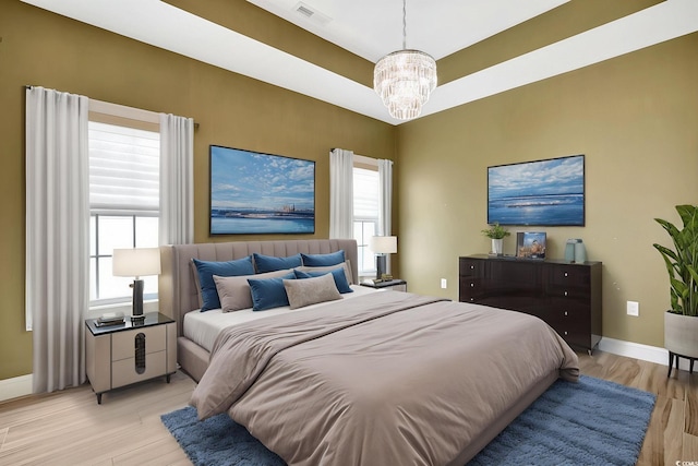 bedroom with light wood finished floors, visible vents, a notable chandelier, and baseboards