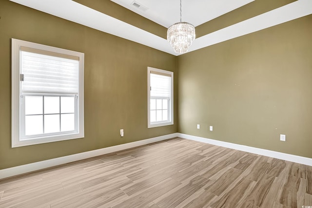 spare room featuring visible vents, light wood-style flooring, a chandelier, and baseboards