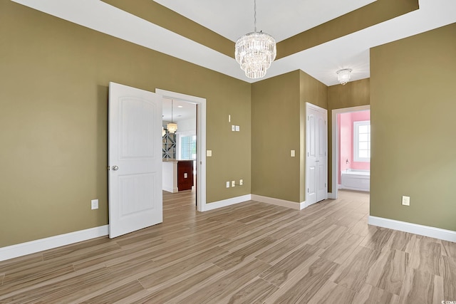spare room with baseboards, an inviting chandelier, and light wood-style floors