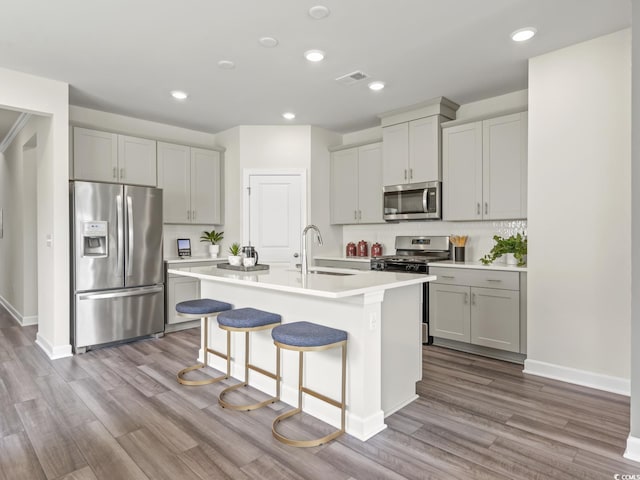 kitchen featuring wood finished floors, an island with sink, light countertops, a sink, and stainless steel appliances