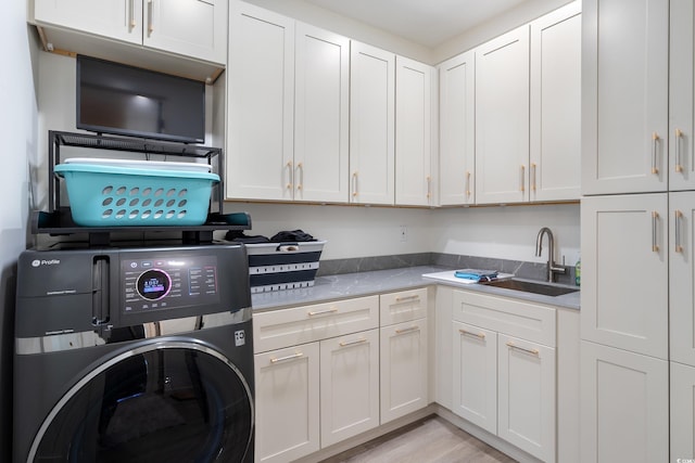 clothes washing area with cabinet space, washer / dryer, a sink, and light wood-style flooring