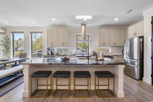 kitchen with a sink, light wood-style floors, freestanding refrigerator, dark stone counters, and a kitchen bar