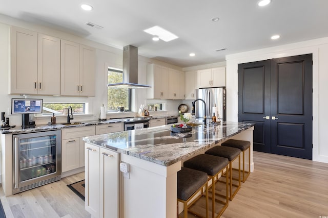 kitchen with wine cooler, light wood-style floors, island range hood, a kitchen bar, and a sink