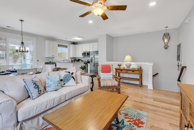 living area featuring recessed lighting, light wood finished floors, and ceiling fan with notable chandelier