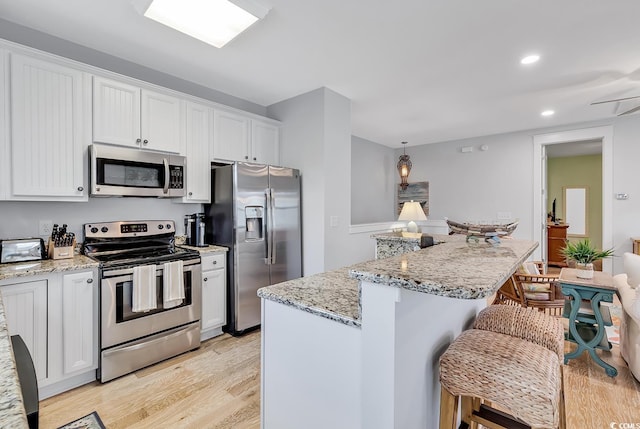 kitchen with light wood-style floors, a breakfast bar area, a center island, white cabinetry, and appliances with stainless steel finishes
