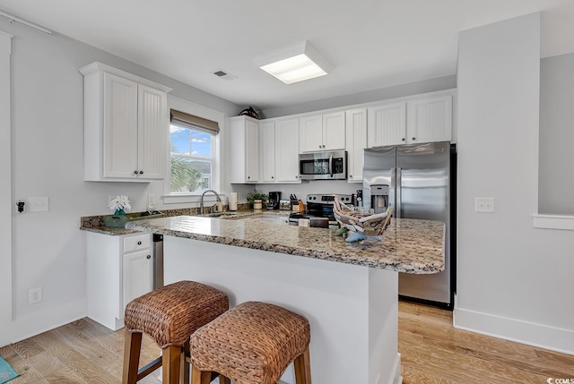 kitchen with stainless steel appliances, light wood finished floors, white cabinetry, and visible vents