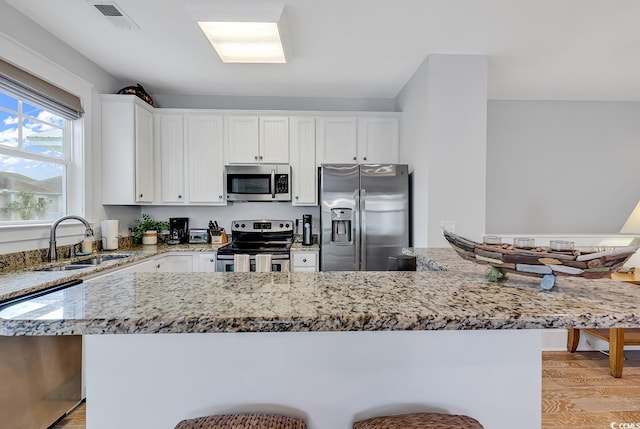 kitchen with light stone countertops, appliances with stainless steel finishes, a sink, white cabinetry, and visible vents