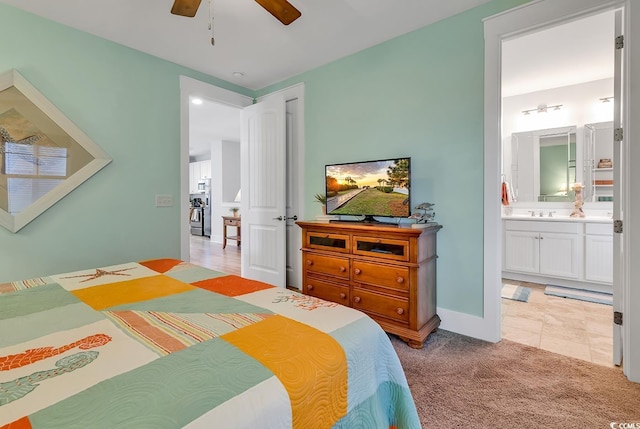 bedroom with baseboards, light carpet, a ceiling fan, and ensuite bath
