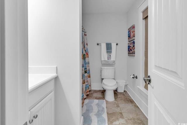 bathroom featuring a shower with curtain, stone finish flooring, baseboards, vanity, and toilet