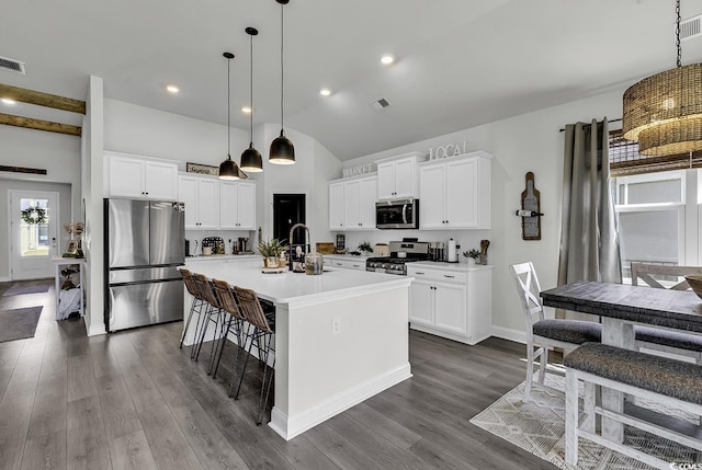 kitchen with an island with sink, dark wood-style floors, hanging light fixtures, and stainless steel appliances