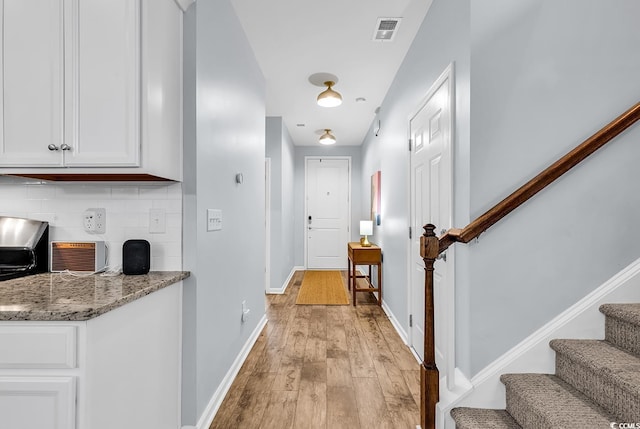 corridor with baseboards, stairs, light wood-style flooring, and visible vents