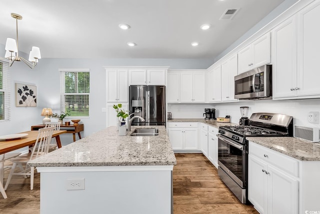 kitchen with appliances with stainless steel finishes, a sink, an island with sink, white cabinetry, and visible vents