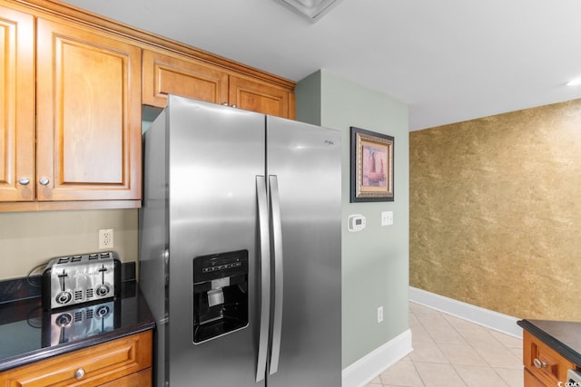 kitchen with dark countertops, baseboards, stainless steel fridge, brown cabinets, and light tile patterned floors