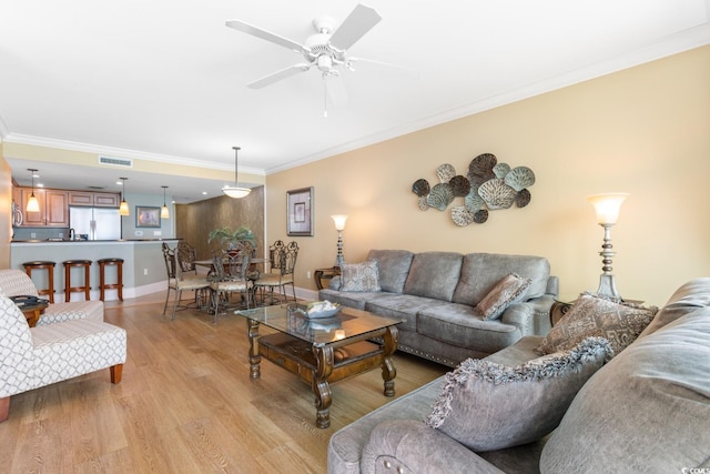 living area featuring crown molding, visible vents, baseboards, ceiling fan, and light wood-type flooring