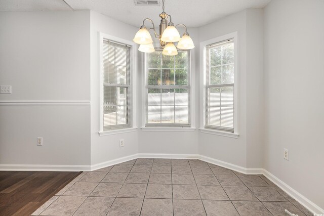 unfurnished dining area with tile patterned flooring, baseboards, a chandelier, and visible vents