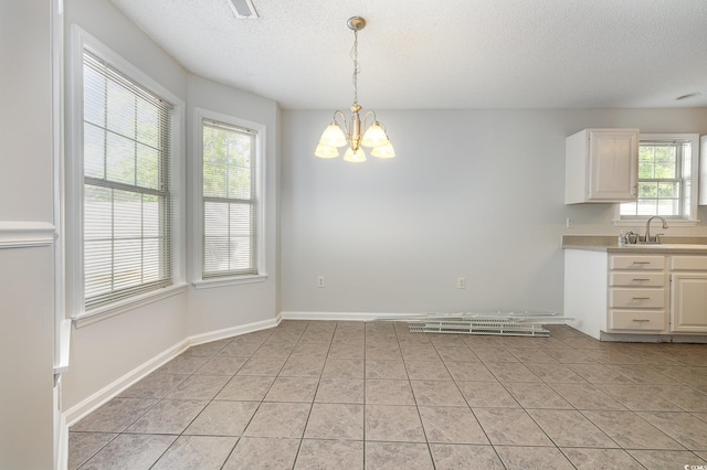unfurnished dining area featuring a sink, a textured ceiling, an inviting chandelier, and light tile patterned floors