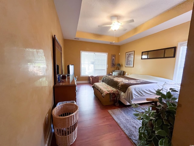 bedroom featuring a ceiling fan, wood finished floors, and a raised ceiling
