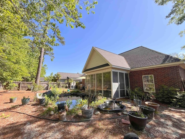 rear view of property with fence, a sunroom, roof with shingles, and brick siding