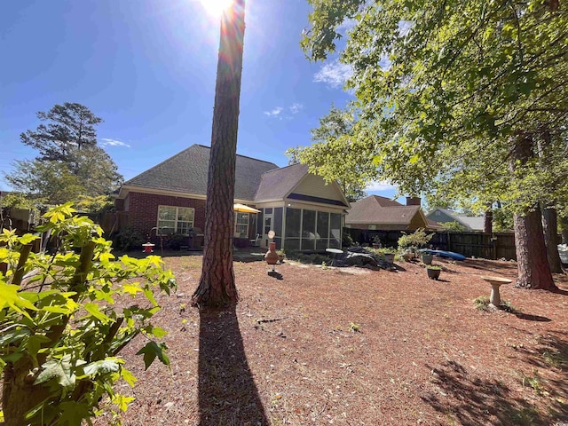 back of house featuring fence, a shingled roof, and a sunroom
