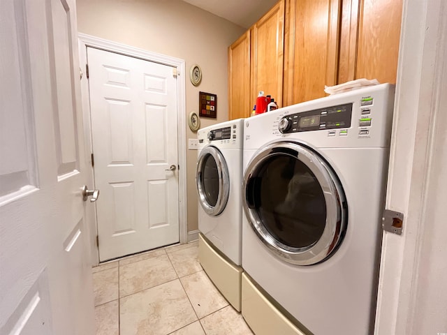 clothes washing area featuring cabinet space, light tile patterned floors, and washing machine and dryer