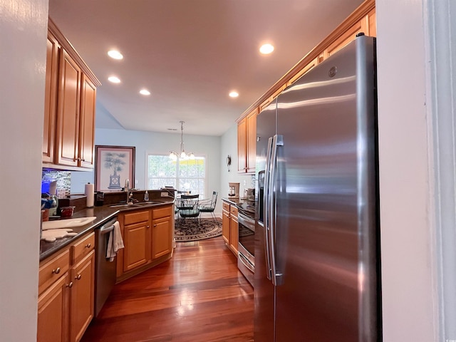 kitchen with dark countertops, appliances with stainless steel finishes, a sink, recessed lighting, and dark wood-type flooring