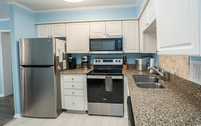 kitchen featuring crown molding, a sink, dark stone countertops, stainless steel appliances, and white cabinetry