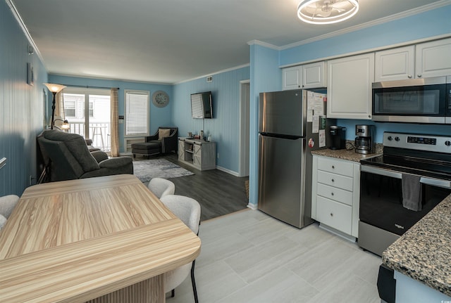 kitchen with crown molding, appliances with stainless steel finishes, white cabinets, stone countertops, and open floor plan