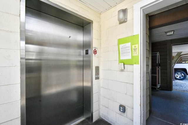 room details featuring concrete block wall, elevator, and concrete floors