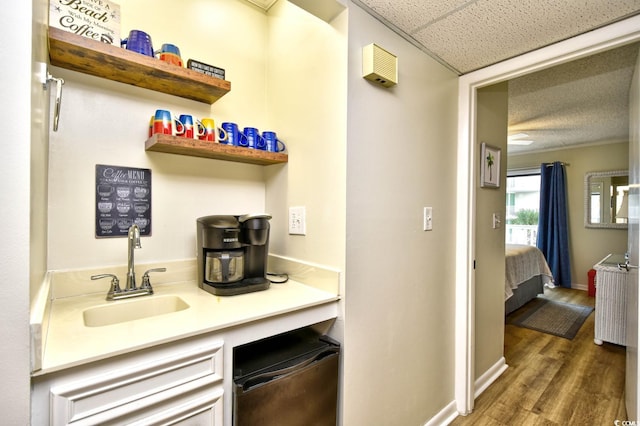 bar featuring a paneled ceiling, baseboards, a sink, and wood finished floors