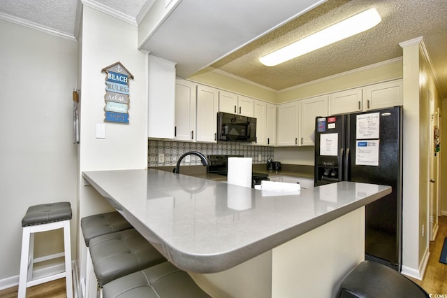 kitchen with a peninsula, a textured ceiling, white cabinetry, and black appliances