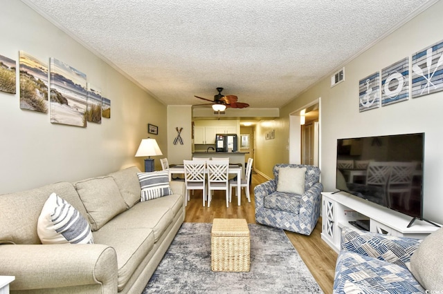 living area featuring crown molding, ceiling fan, light wood finished floors, and a textured ceiling