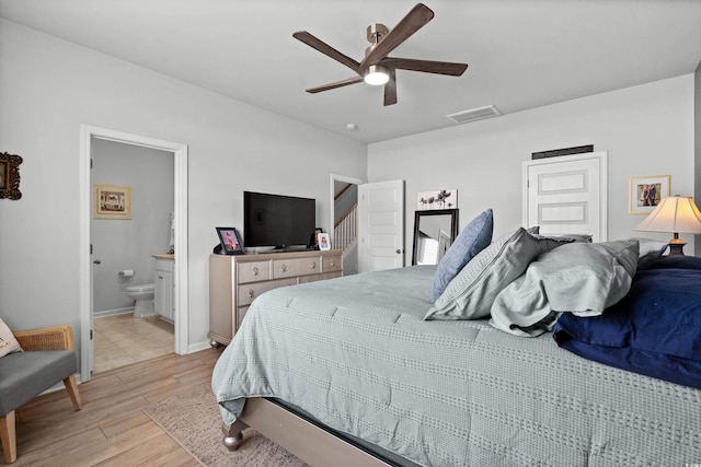 bedroom featuring ceiling fan, visible vents, baseboards, light wood-style floors, and ensuite bathroom