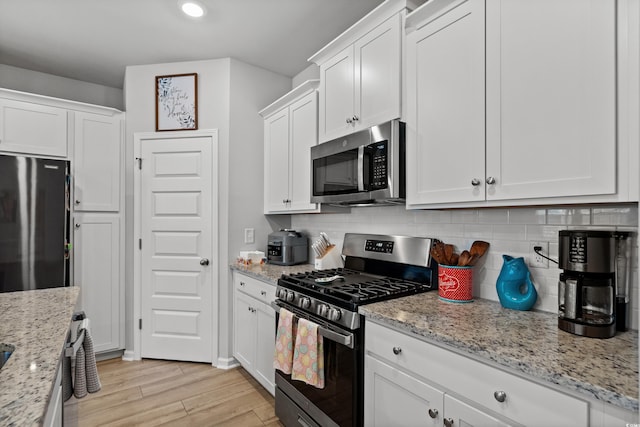 kitchen with white cabinets, light stone counters, light wood finished floors, backsplash, and stainless steel appliances