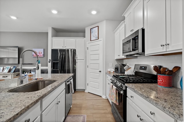 kitchen with appliances with stainless steel finishes, a sink, light wood-style flooring, white cabinetry, and backsplash
