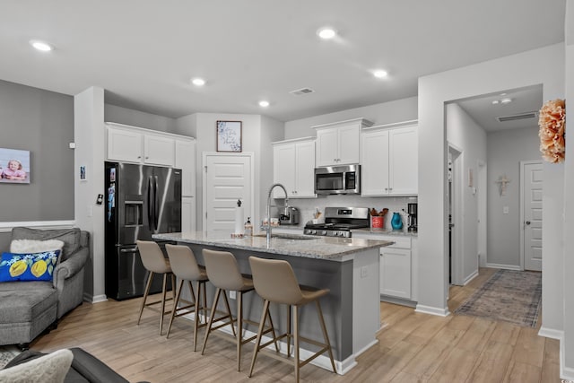 kitchen featuring a kitchen breakfast bar, white cabinets, a sink, light wood-style flooring, and stainless steel appliances
