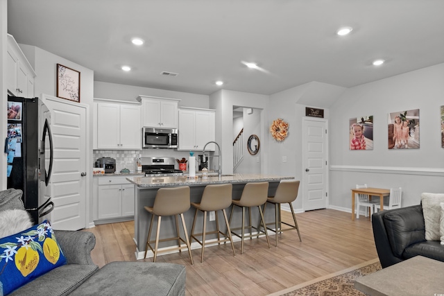 kitchen with visible vents, open floor plan, a kitchen bar, light wood-type flooring, and appliances with stainless steel finishes