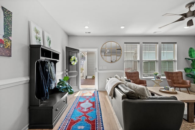 living room featuring ceiling fan, visible vents, baseboards, and light wood finished floors