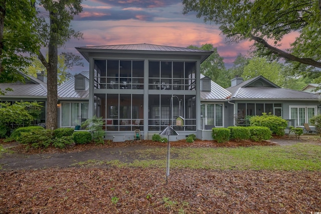 rear view of house with a standing seam roof, a chimney, a sunroom, and metal roof