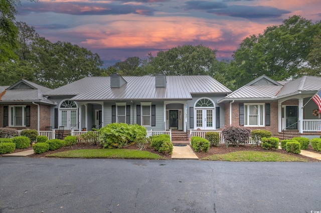 view of front of house with french doors, a porch, metal roof, and brick siding