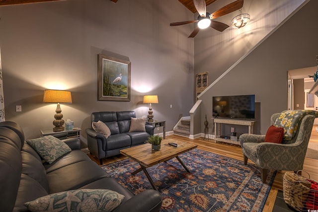 living area with a ceiling fan, a towering ceiling, wood finished floors, baseboards, and stairs