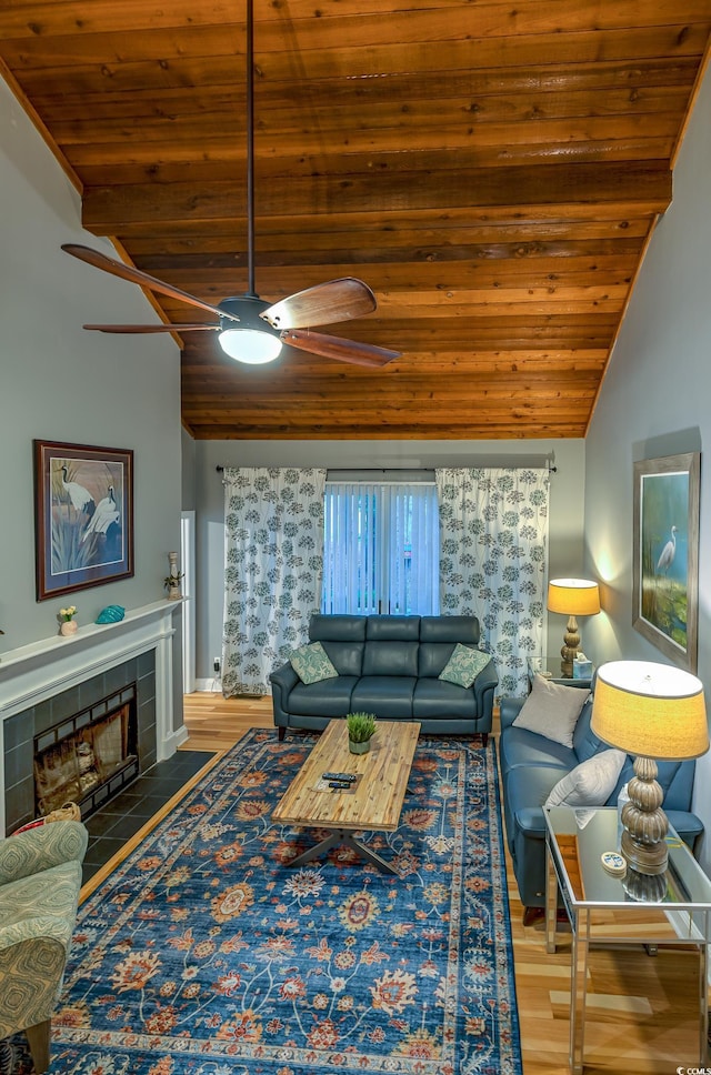 living area with ceiling fan, a tiled fireplace, wood finished floors, vaulted ceiling, and wood ceiling