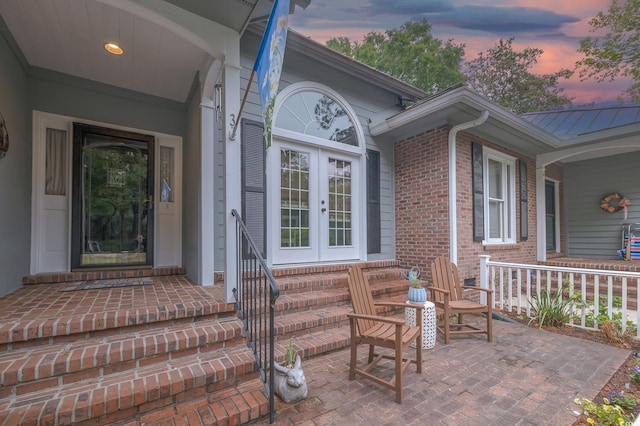 property entrance with french doors, covered porch, metal roof, and brick siding