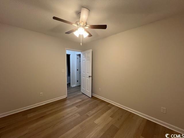 spare room with baseboards, a ceiling fan, and dark wood-style flooring