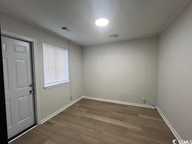 empty room featuring baseboards, ornamental molding, wood finished floors, and visible vents
