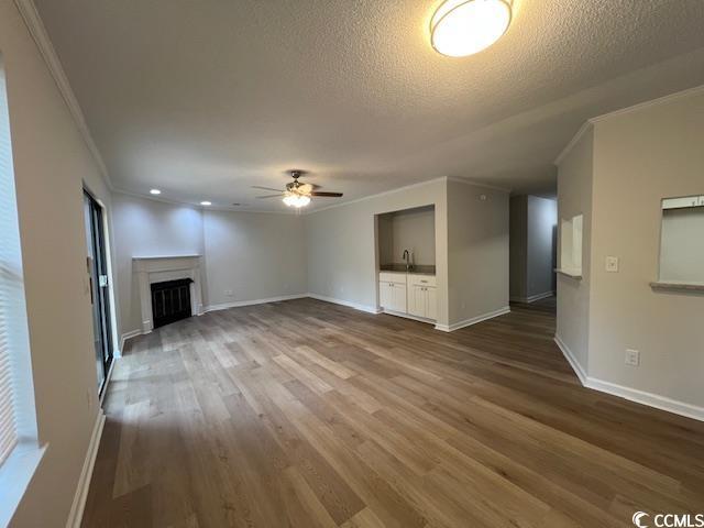 unfurnished living room featuring dark wood-style flooring, ceiling fan, ornamental molding, and a fireplace